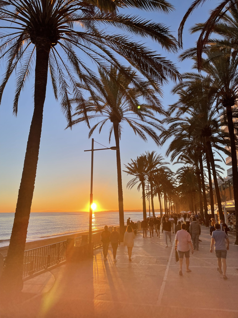 People walking the Marbella paseo marítimo under palms at sunset